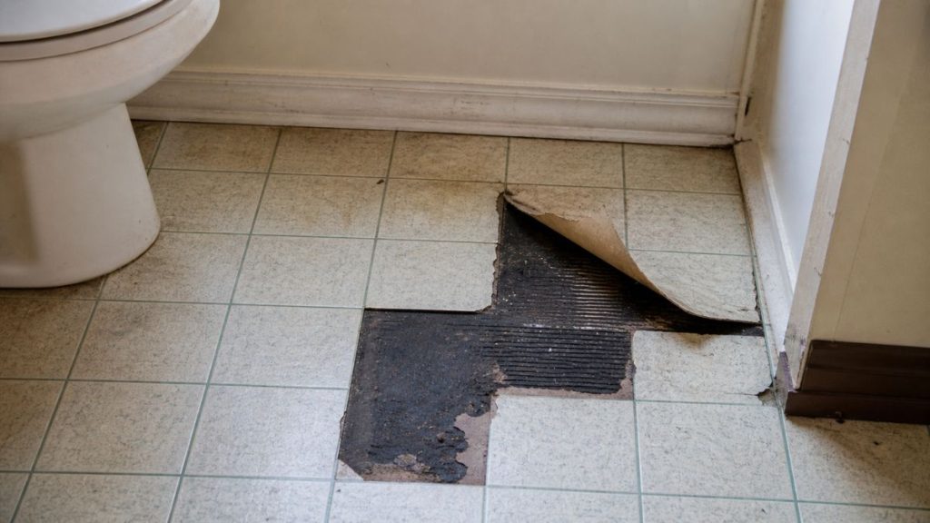 Old vinyl floor tiles with a lifted section revealing black adhesive, a common area where asbestos may be found in older homes